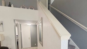 A hallway with a staircase leading to an upper floor, a door at the end, and a brown chair on the left.