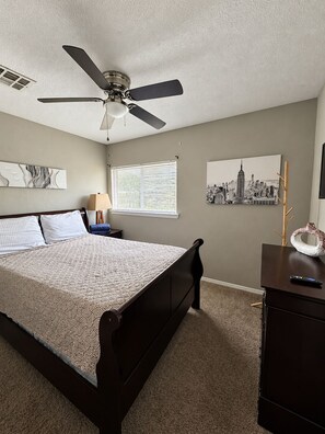 A bedroom with a bed, a ceiling fan, a window with blinds, and wall art.