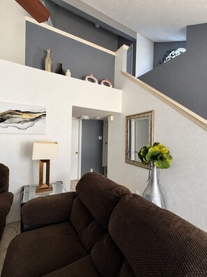 A living room with a sofa, a lamp, a vase with flowers, and a mirror on the wall.