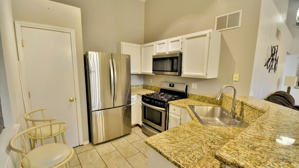 A kitchen with white cabinets, stainless steel appliances, granite countertops, and a double sink.
