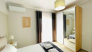 A hotel room with a bed, a bedside table with a lamp, a large mirror, and a window with curtains. - Nova City Center - 217 (Divjakë)