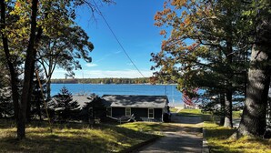 A cabin with a gravel driveway leading to a dock by a lake.