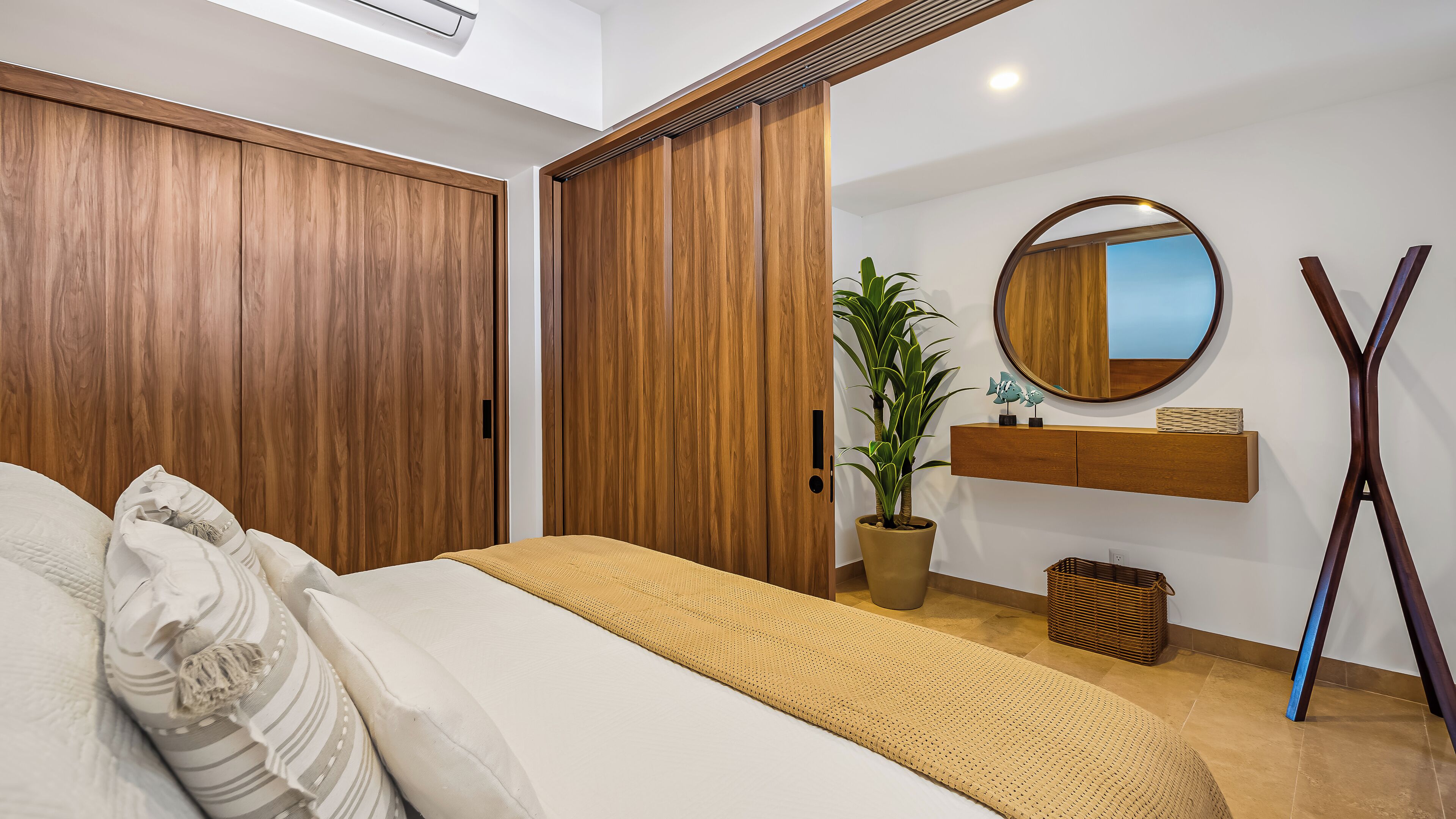 Un dormitorio con una cama, un espejo grande, una planta en maceta y armarios de madera.