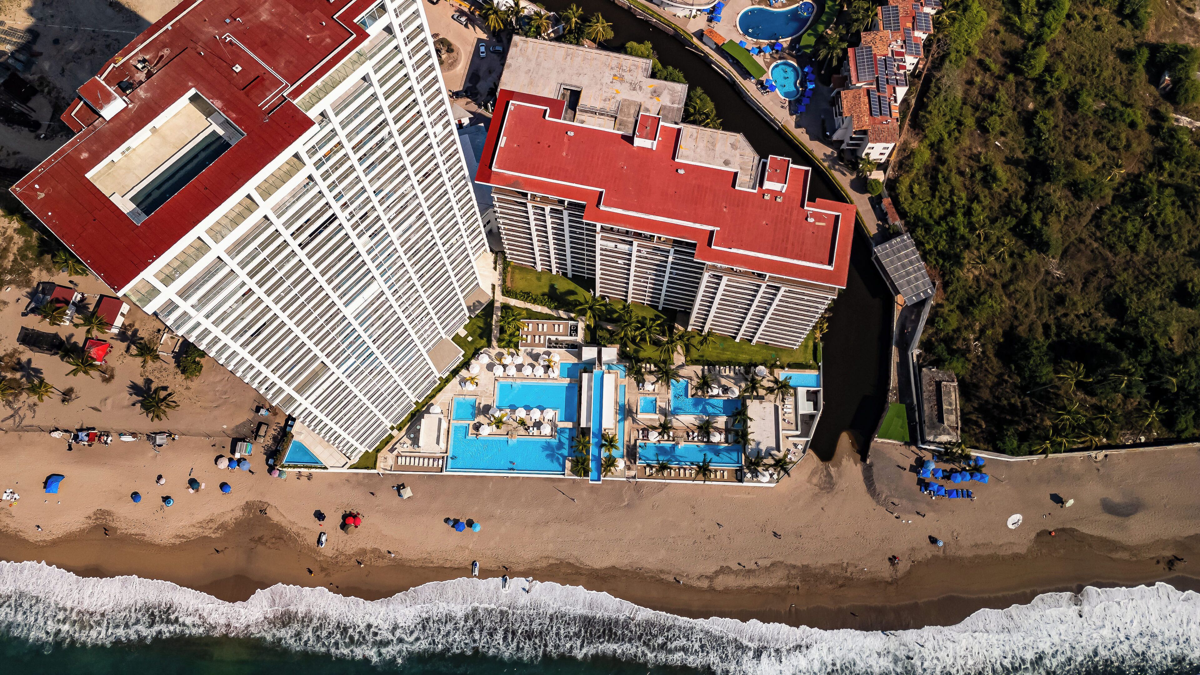 An aerial view of a resort with multiple swimming pools, a beach, and a large hotel building.