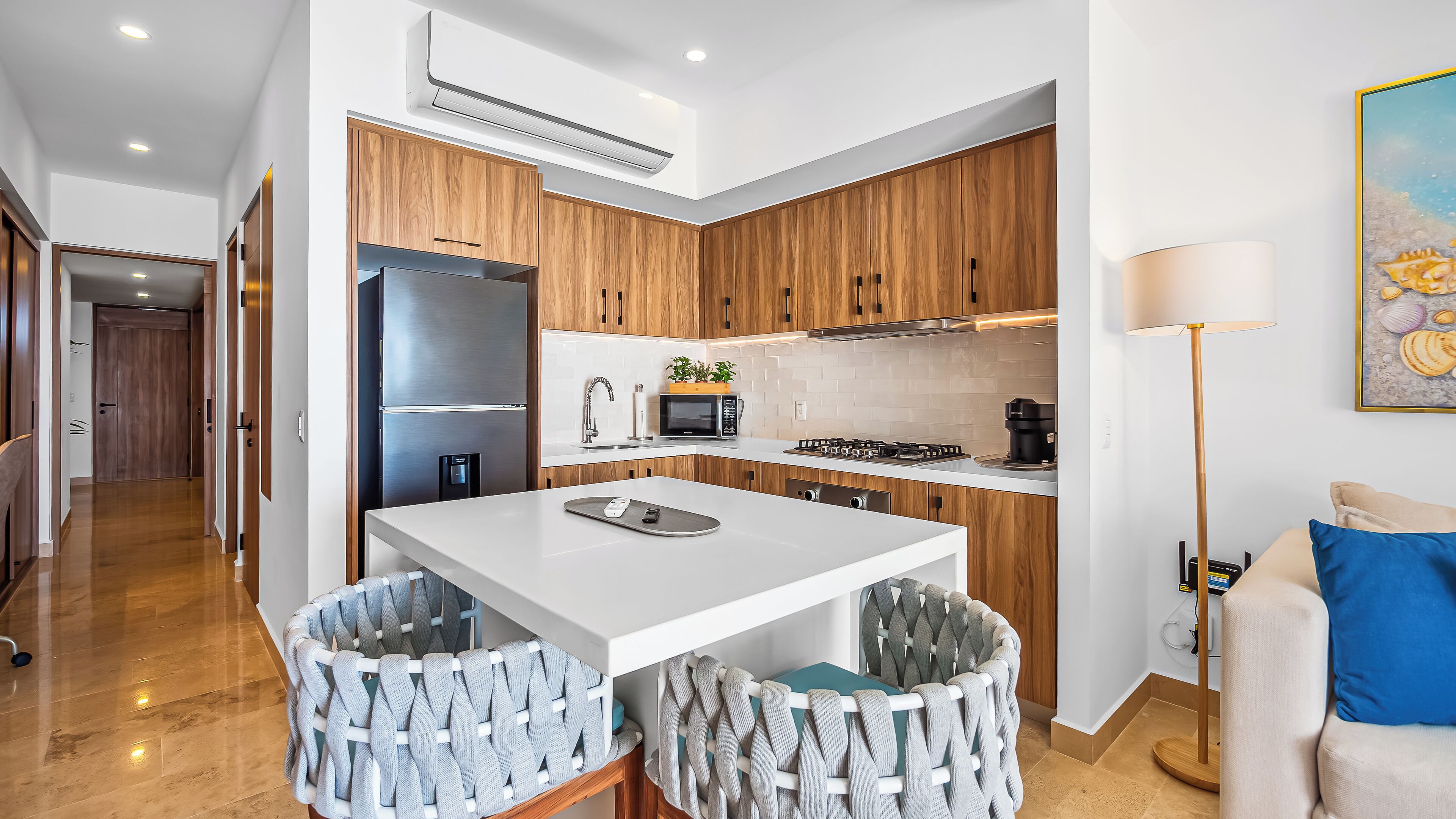 A modern kitchen with wooden cabinets, a white countertop, and a built-in stove. There is a refrigerator, a microwave, and a sink.