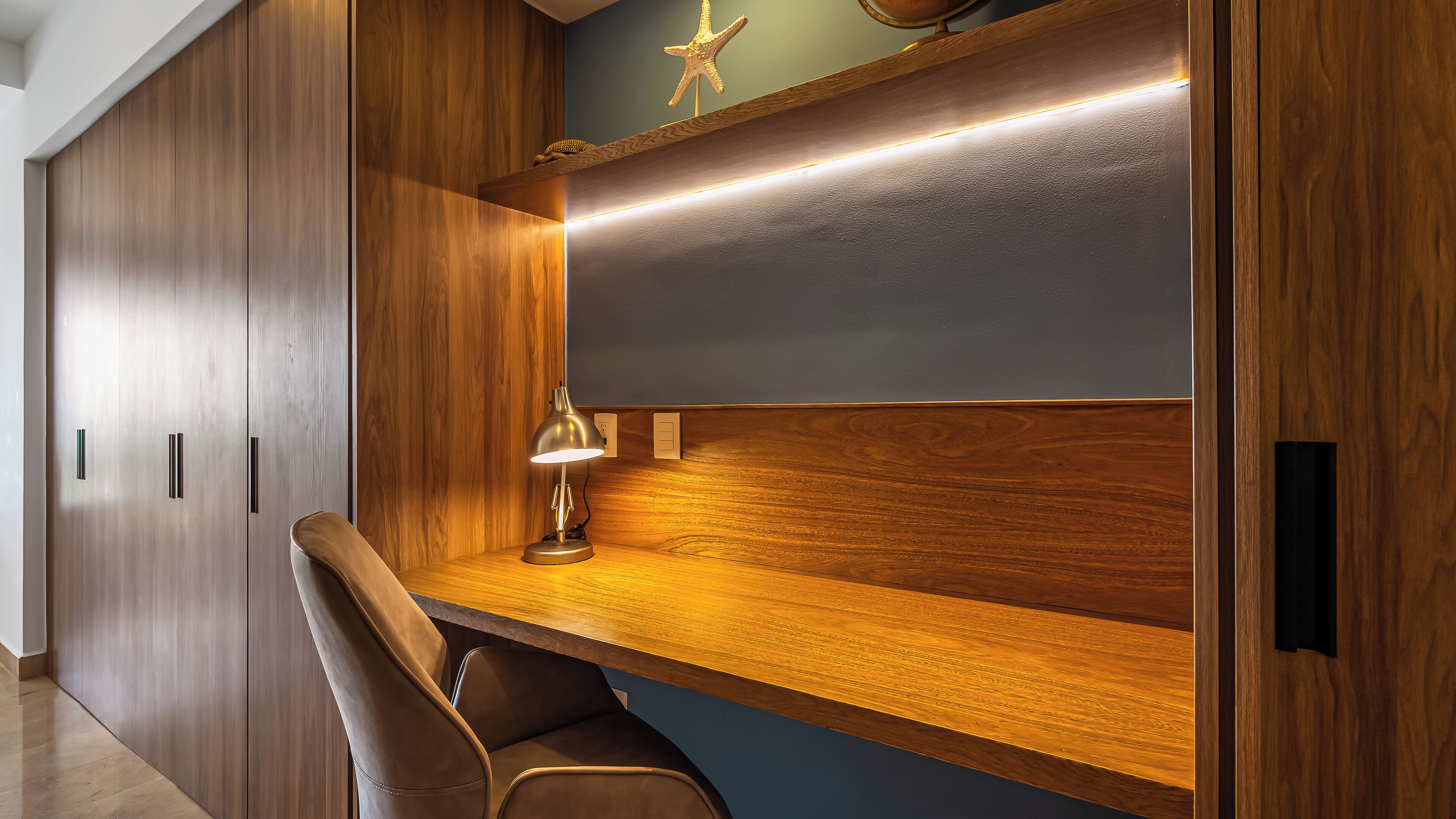 A modern office space with a wooden desk, a leather chair, and a desk lamp.