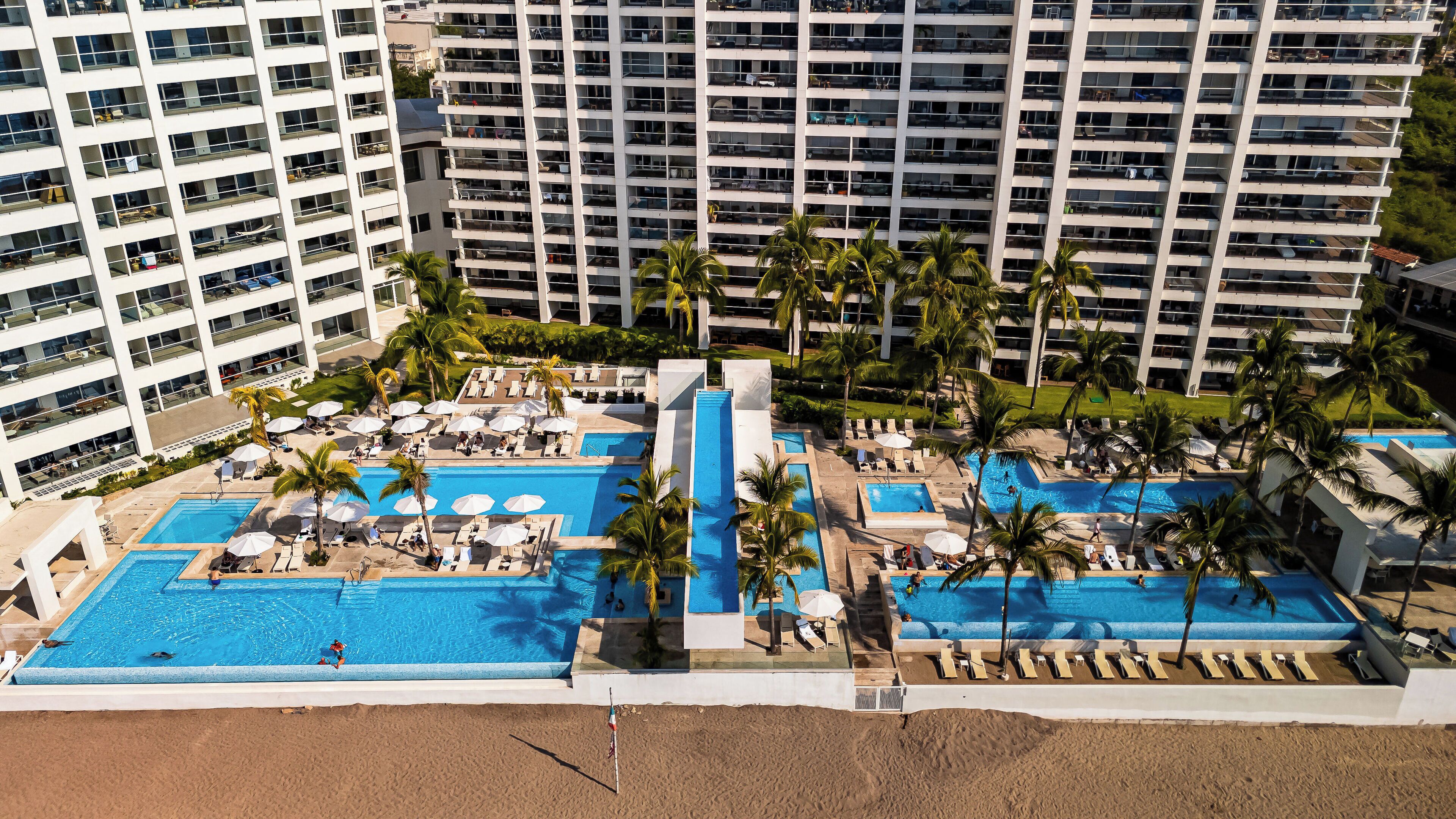A resort with multiple swimming pools, palm trees, and a beach area.