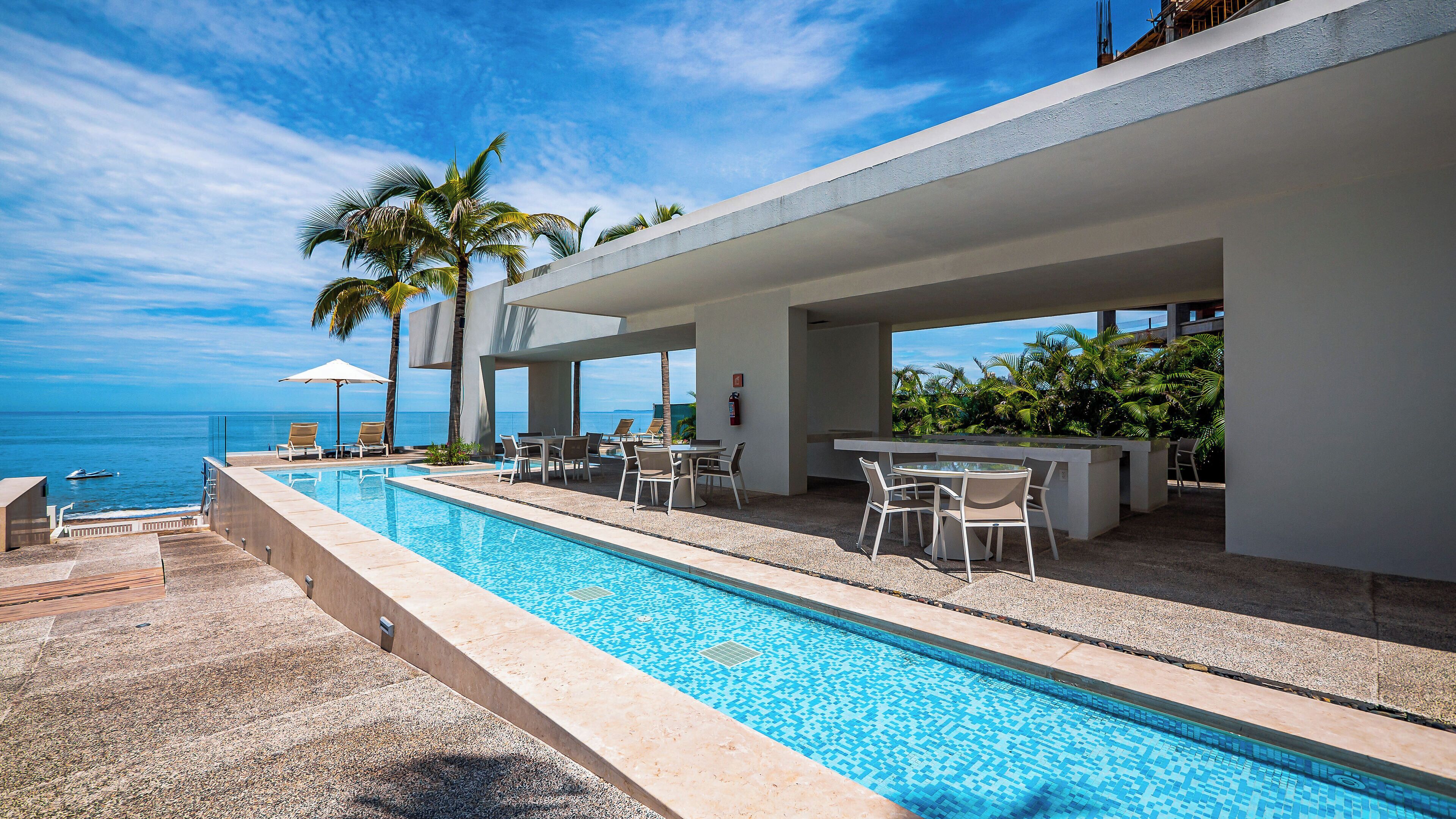 A swimming pool with lounge chairs and tables, overlooking the ocean.