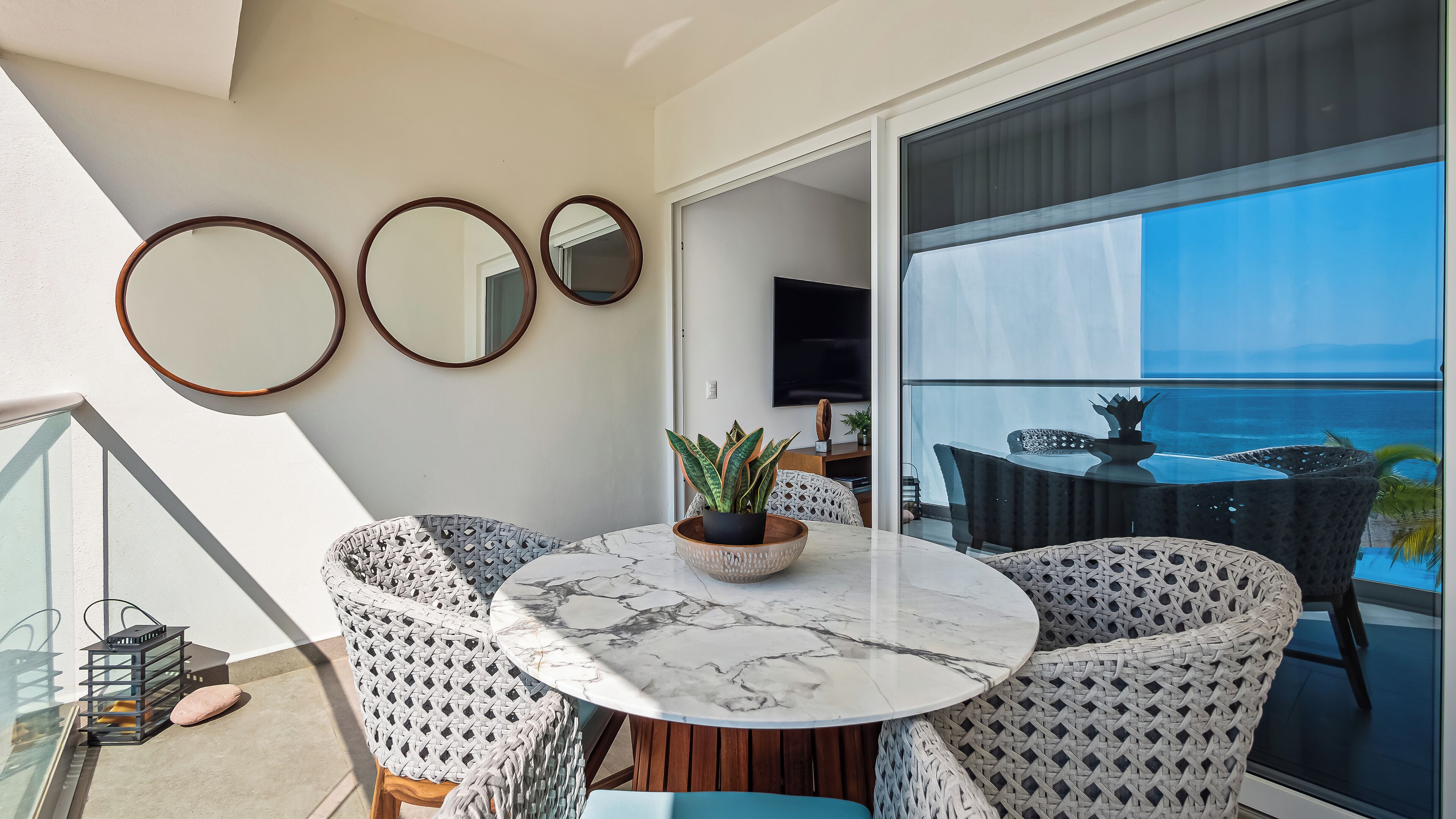 A balcony with a round table, wicker chairs, and a potted plant.