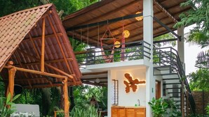 A two-story building with a pool, a wooden deck, and a balcony with hanging lights.