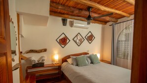 A bedroom with a wooden ceiling, a bed with white bedding, a nightstand with a lamp, and wall-mounted artwork.