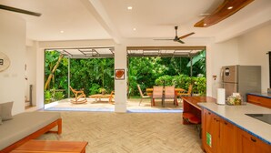 A modern interior with a wooden floor, a sofa, a dining area with chairs, a ceiling fan, and a kitchen with a refrigerator.