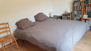 A bedroom with a bed, a wooden chair, a nightstand with a lamp, and a bookshelf filled with books. - Quiet house close to all amenities and train station (Chauffailles)