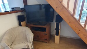 A living room with a television on a wooden stand, a beige sofa, and a wooden staircase. - Quiet house close to all amenities and train station (Chauffailles)