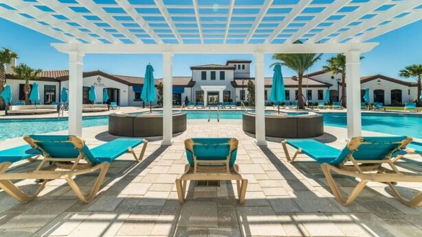 Zwembadgedeelte met ligbedden en parasols, een overdekte pergola en een gebouw op de achtergrond.