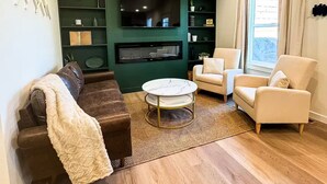 En moderne stue med et fladskærms-tv monteret på en grøn væg, en brun lædersofa, en hvid lænestol og et sofabord.