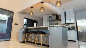 Een moderne keuken met een centraal eiland, barstoelen, hanglampen en roestvrijstalen apparatuur.