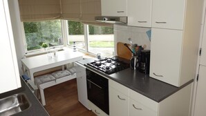 A compact kitchen with white cabinets, a gas stove, a sink, and a window overlooking a garden. - Bungalow in Sint Maartenszee Near Beach (Sint Maartensvlotbrug)