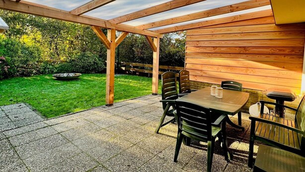 A wooden pergola with a table and chairs, set on a patio with a view of a garden. - Bungalow in Sint Maartenszee Near Beach (Sint Maartensvlotbrug)