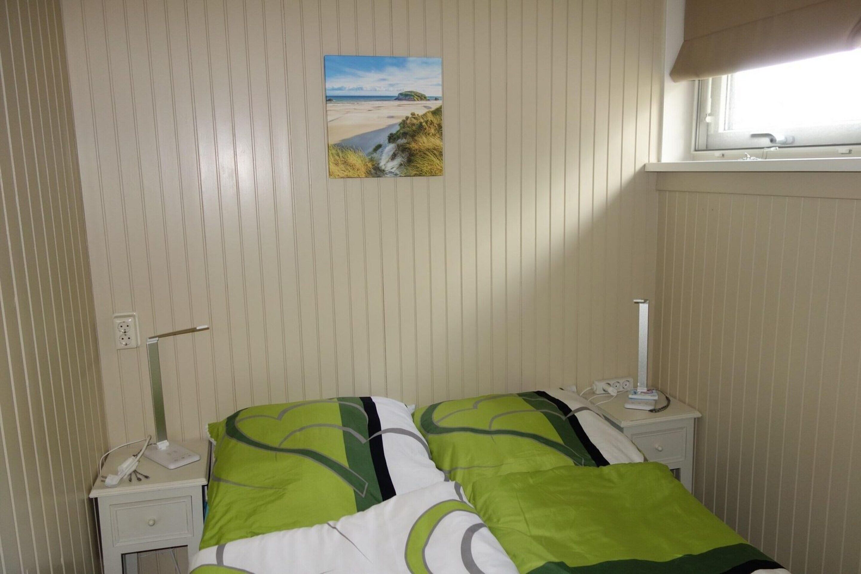 A hotel room with a bed, two bedside tables, a nightstand, a lamp, a painting of a beach scene, and a window with a view of the beach.