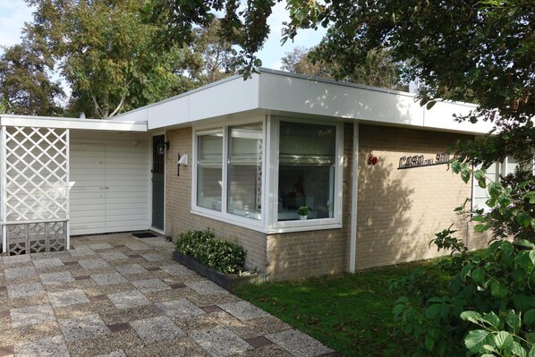 A single-story building with a garage door, a small front porch, and a brick exterior. - Bungalow in Sint Maartenszee Near Beach (Sint Maartensvlotbrug)