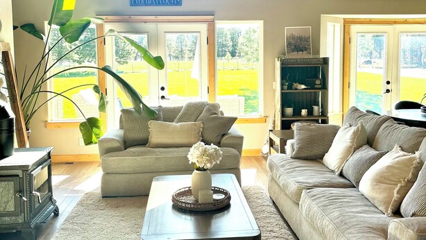 A spacious living room with a high ceiling, a ceiling fan, and large windows offering a view of a green landscape.