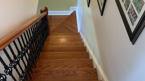 Un escalier en bois avec une rampe noire mène à une pièce dont le mur est d’un vert pâle.