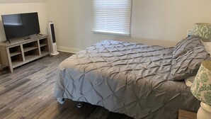 Une chambre à coucher avec un lit, un téléviseur posé sur un meuble, un radiateur et une fenêtre avec des stores.