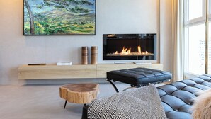 Ein modernes Wohnzimmer mit Kamin, einem großen Landschaftsbild und einer gemütlichen Sitzecke.