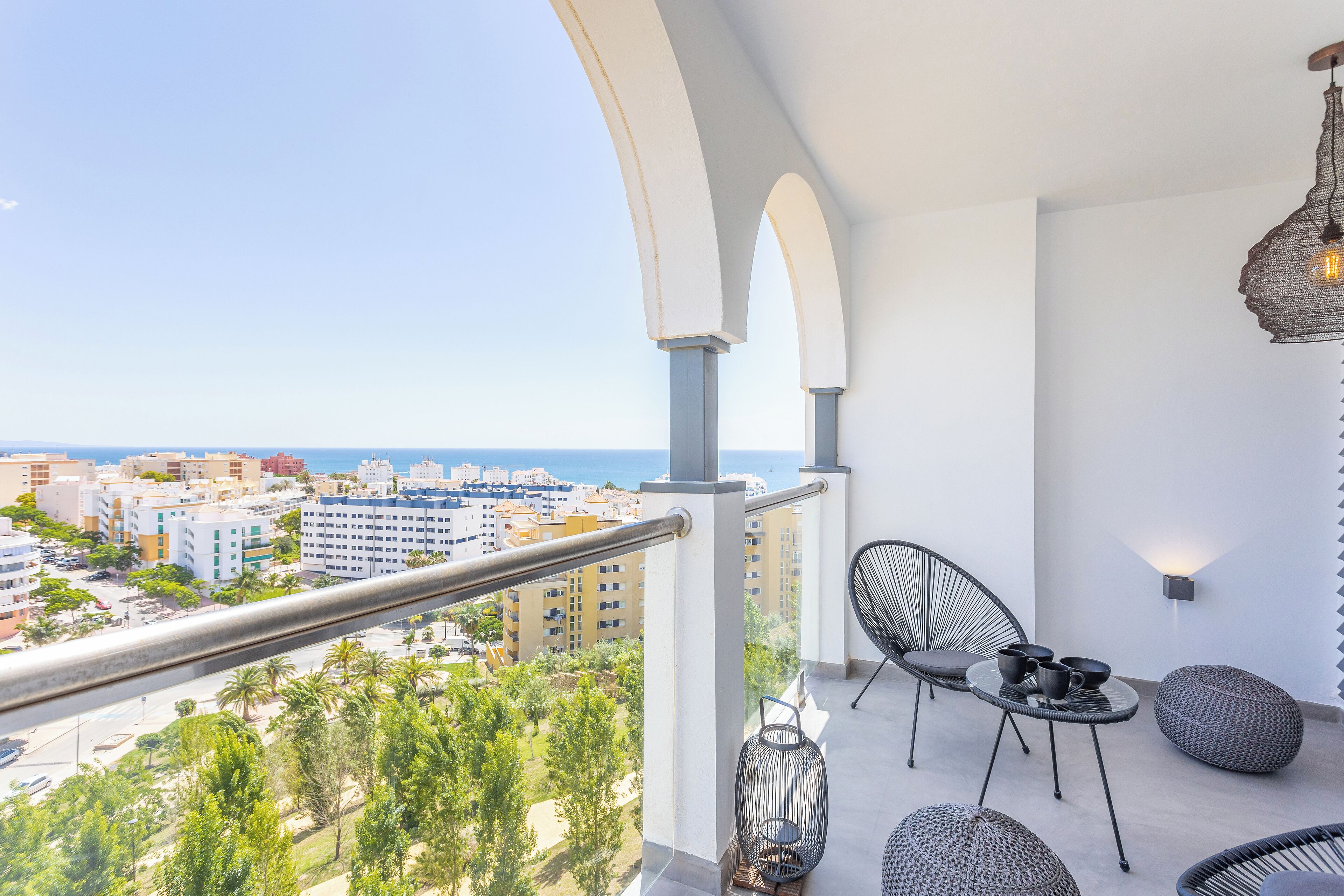 A balcony with a metal railing, wicker chairs, and a table with cups and saucers.