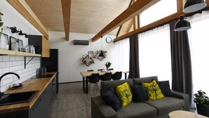 A modern kitchen with wooden beams, a dining area with a table and chairs, and a gray sofa with yellow pillows.
