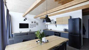 A modern kitchen with wooden beams, a black refrigerator, and a dining table with chairs.