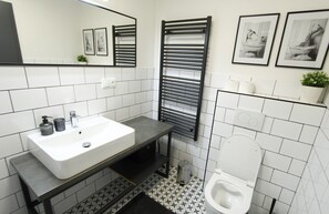 Un baño moderno con un lavamanos blanco, toallero negro y un inodoro.