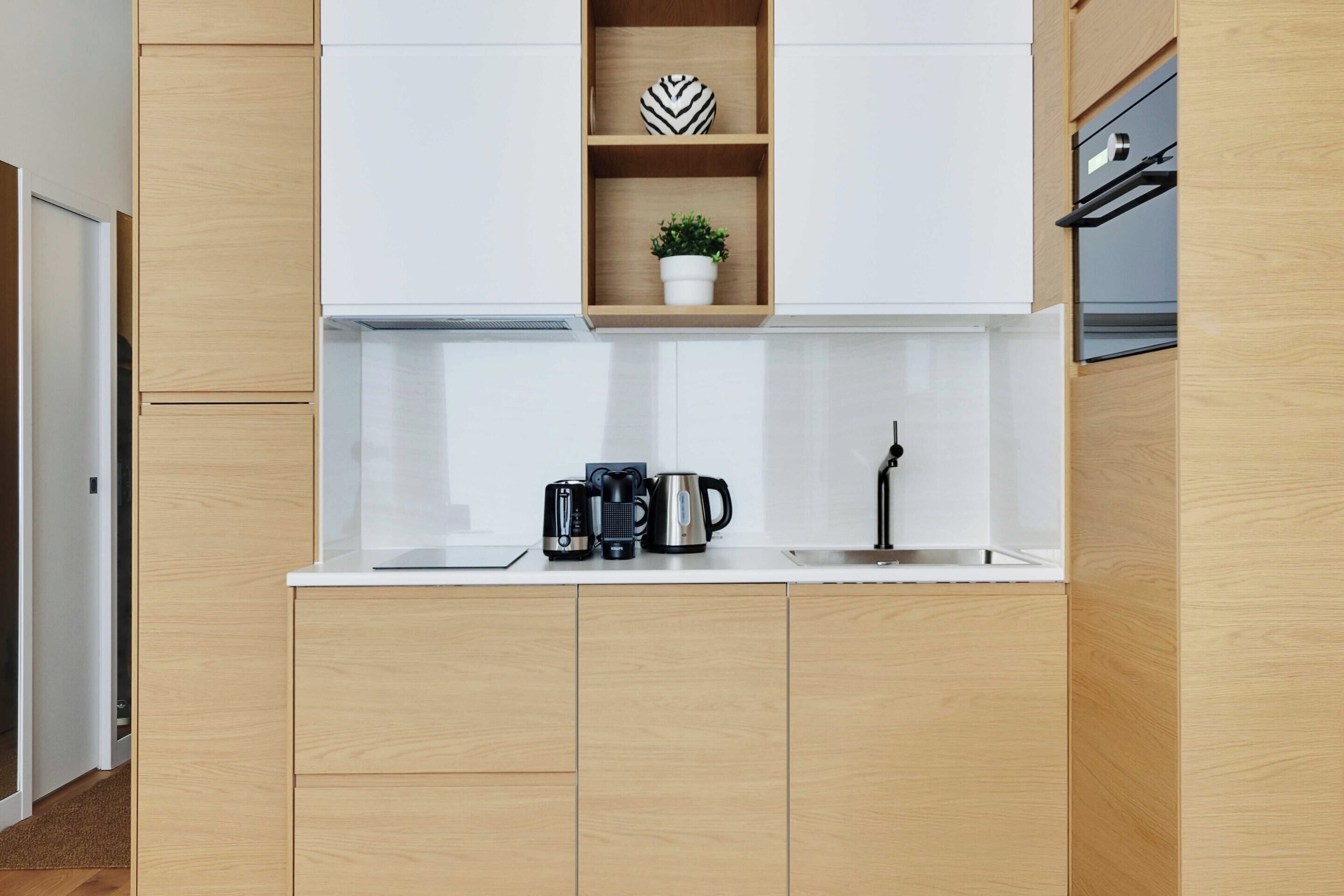 A modern kitchen with wooden cabinets, a white countertop, and a built-in shelf with decorative items.