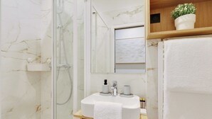 A bathroom with a glass-enclosed shower, a marble wall, a white sink with a towel, and a wooden shelf with a plant. - Charming Apt - 1bd/4p - Invalides/bon Marche (Paris)