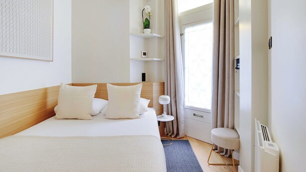A modern hotel room with a large bed, a bedside table, a small side table, a potted plant, and a window with curtains. - Charming Apt - 1bd/4p - Invalides/bon Marche (Paris)