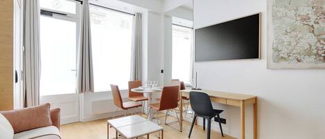 A modern living room with a sofa, a coffee table, a dining table with chairs, and a TV mounted on the wall.