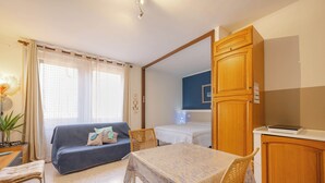 Un espacio habitable compacto con sofá, mesa de comedor, zona de cocina y cama.