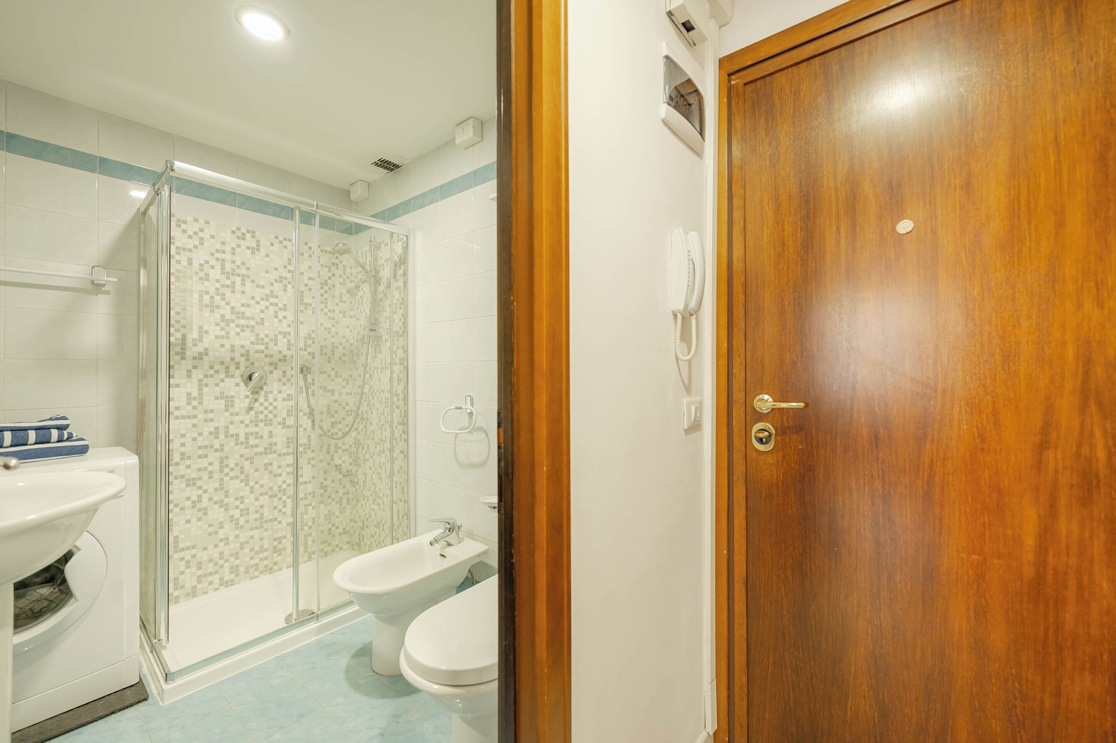 A bathroom with a glass-enclosed shower, two sinks, and a wooden door.