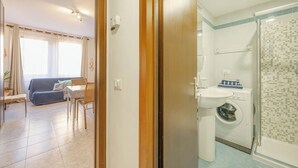 Una habitación con sofá, mesa de comedor con sillas, lavadora y zona de ducha.