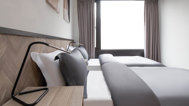A modern hotel room with a wooden headboard, a desk with a chair, two beds with grey bedding, and a large window with curtains. - Taipei Main Station Warm & Cozy 2B1b Living, Dining, Kitchen (Taipei City)