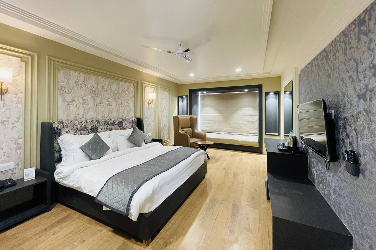 A modern hotel room with a large bed, a seating area, a flat-screen TV, and a minibar.