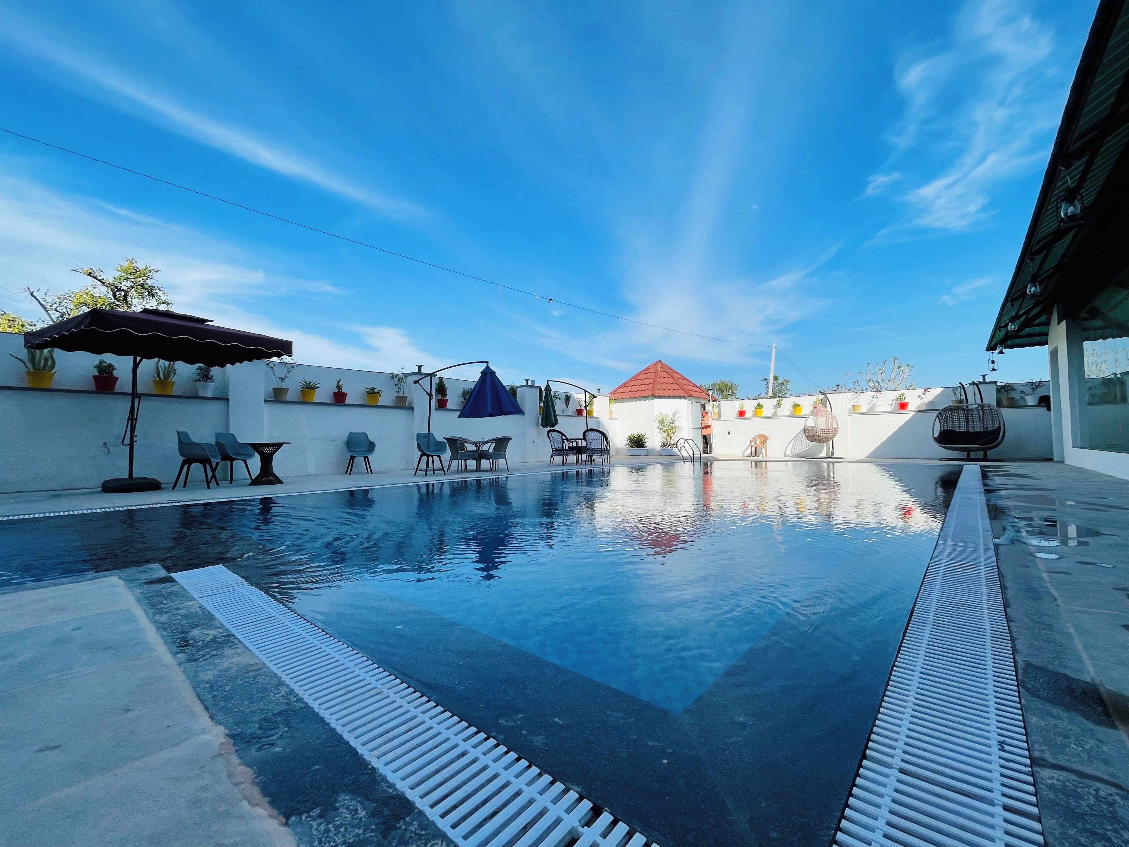 A swimming pool with a white deck, surrounded by outdoor furniture and potted plants.