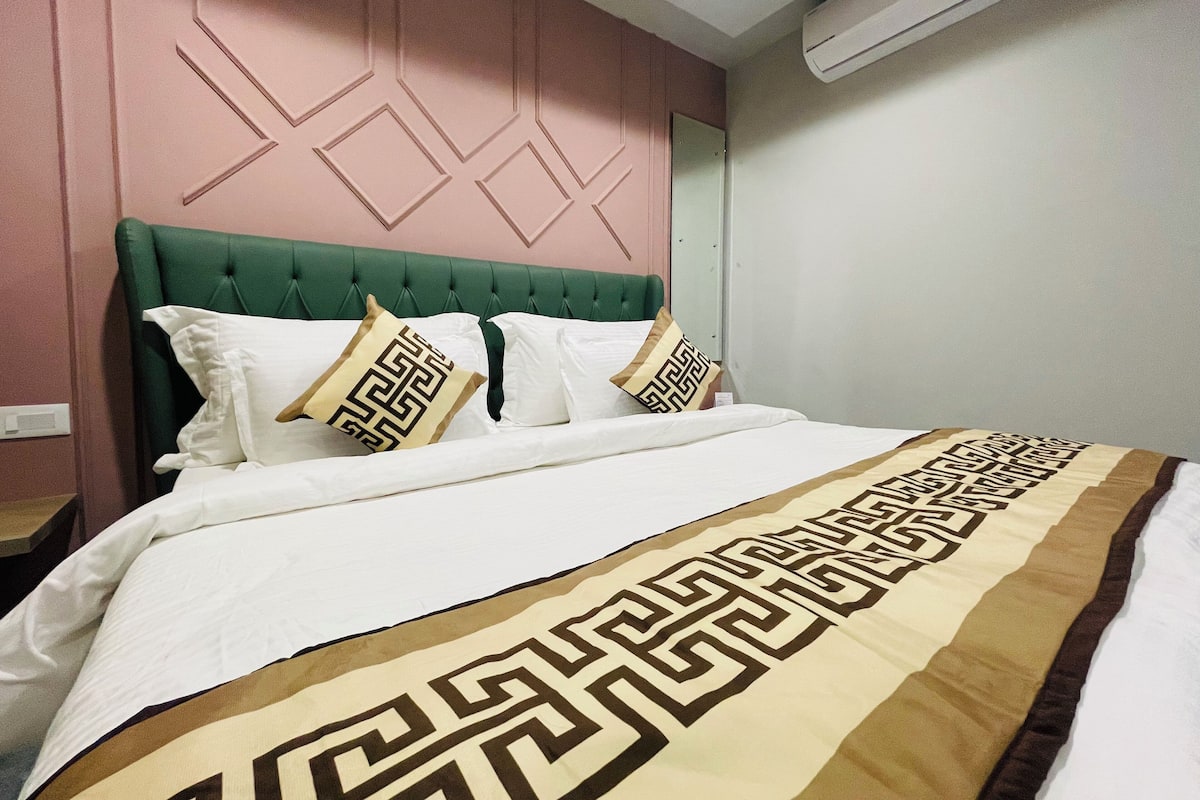 A neatly made bed with a patterned bedspread, a green upholstered headboard, and decorative pillows.