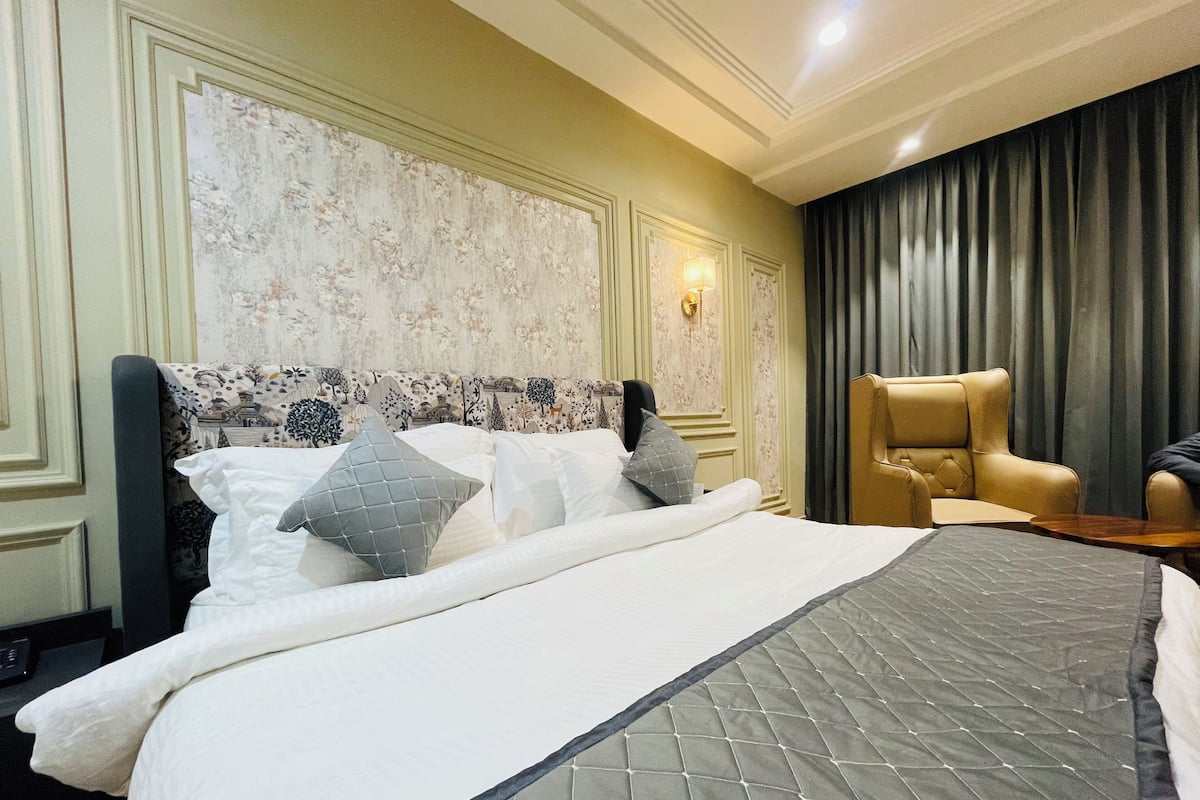 A hotel room with a large bed, a chair, and a wall with a floral pattern.