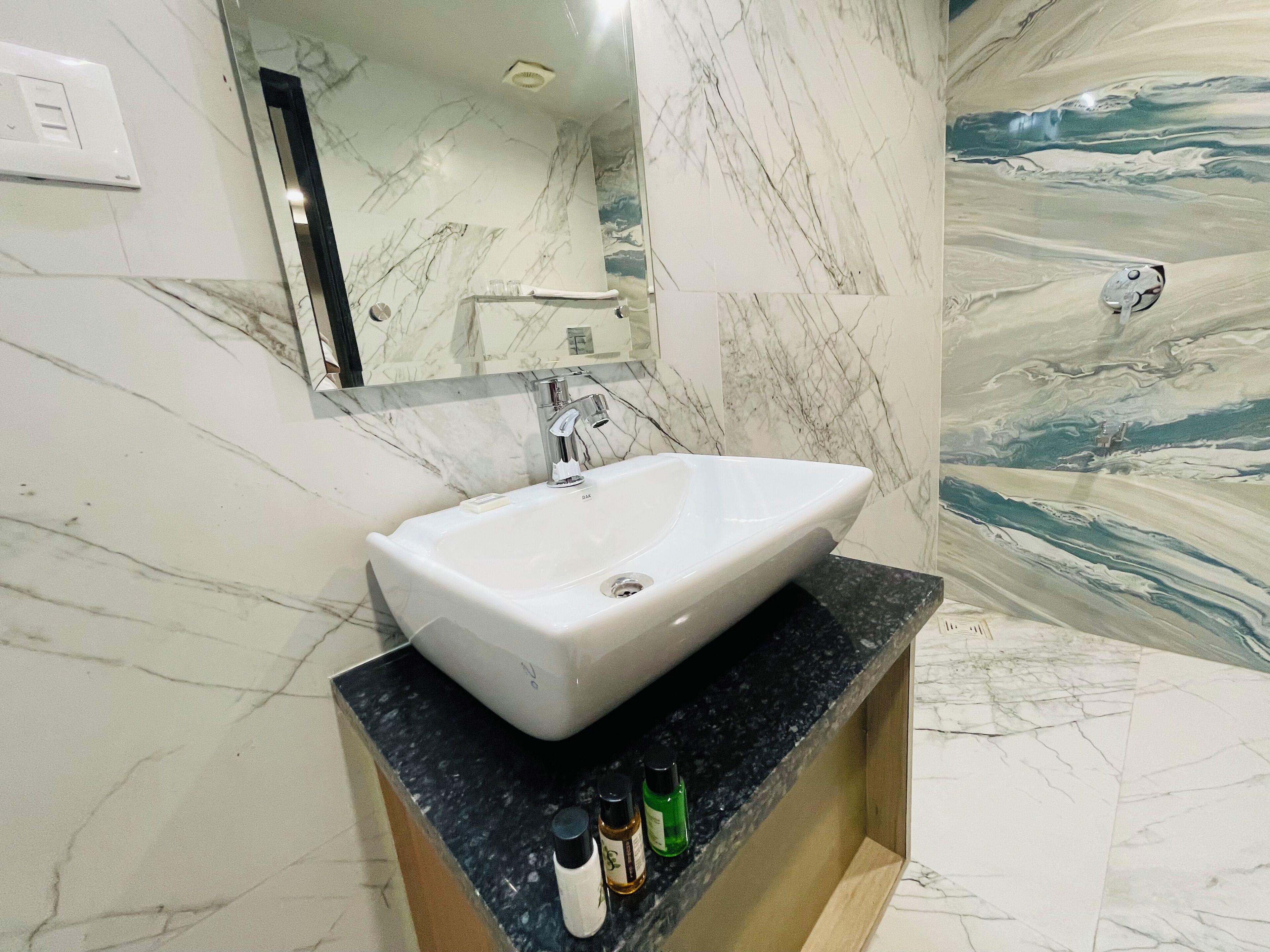 Un baño con lavamanos blanco, paredes de mármol y un espejo.