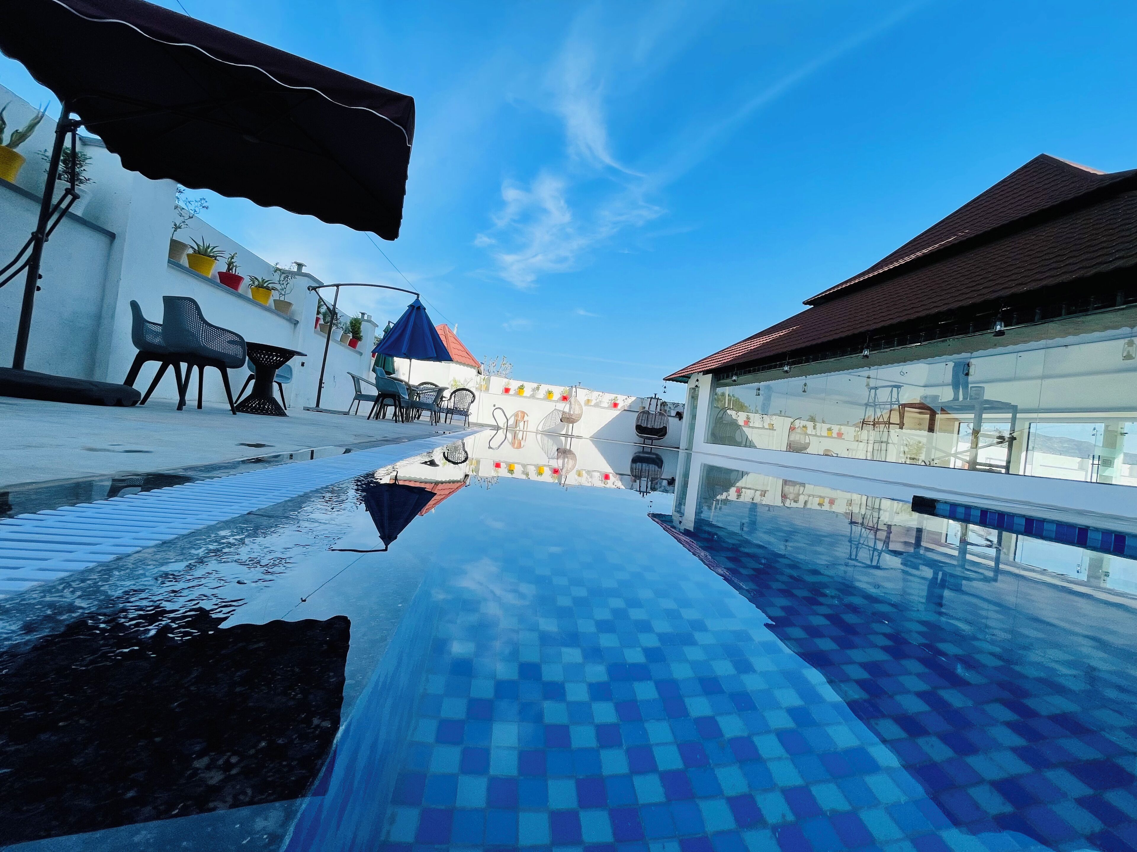 A swimming pool with a checkered pattern, surrounded by outdoor seating and a building with a red roof.