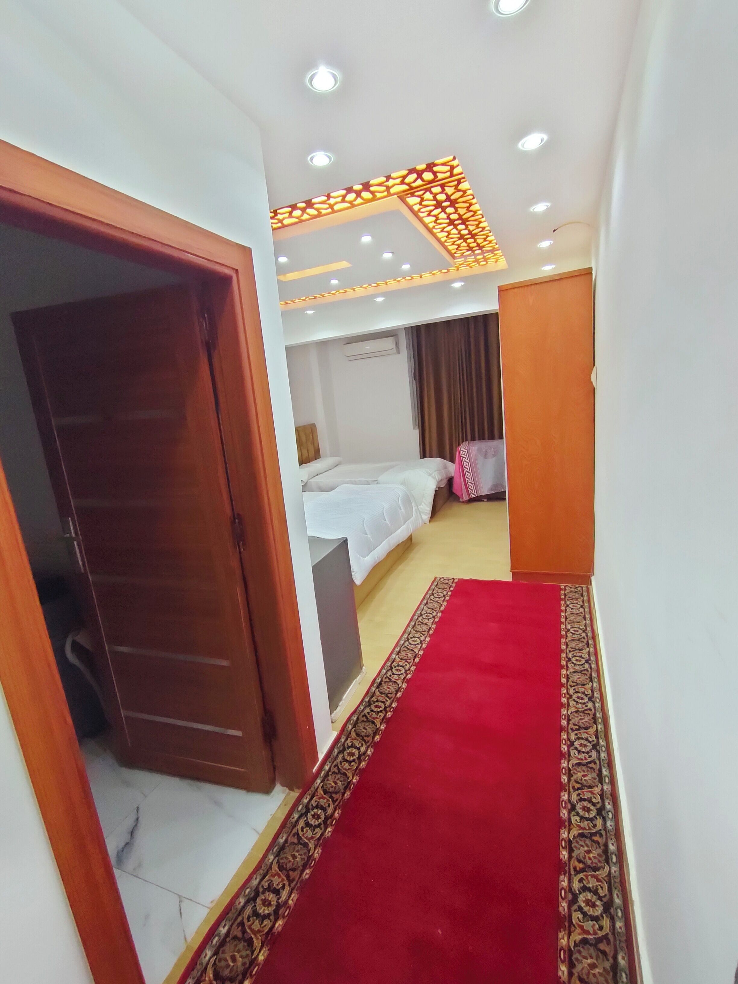 Una camera d'albergo con tappeto rosso, un letto, un armadio e una lampada a soffitto.