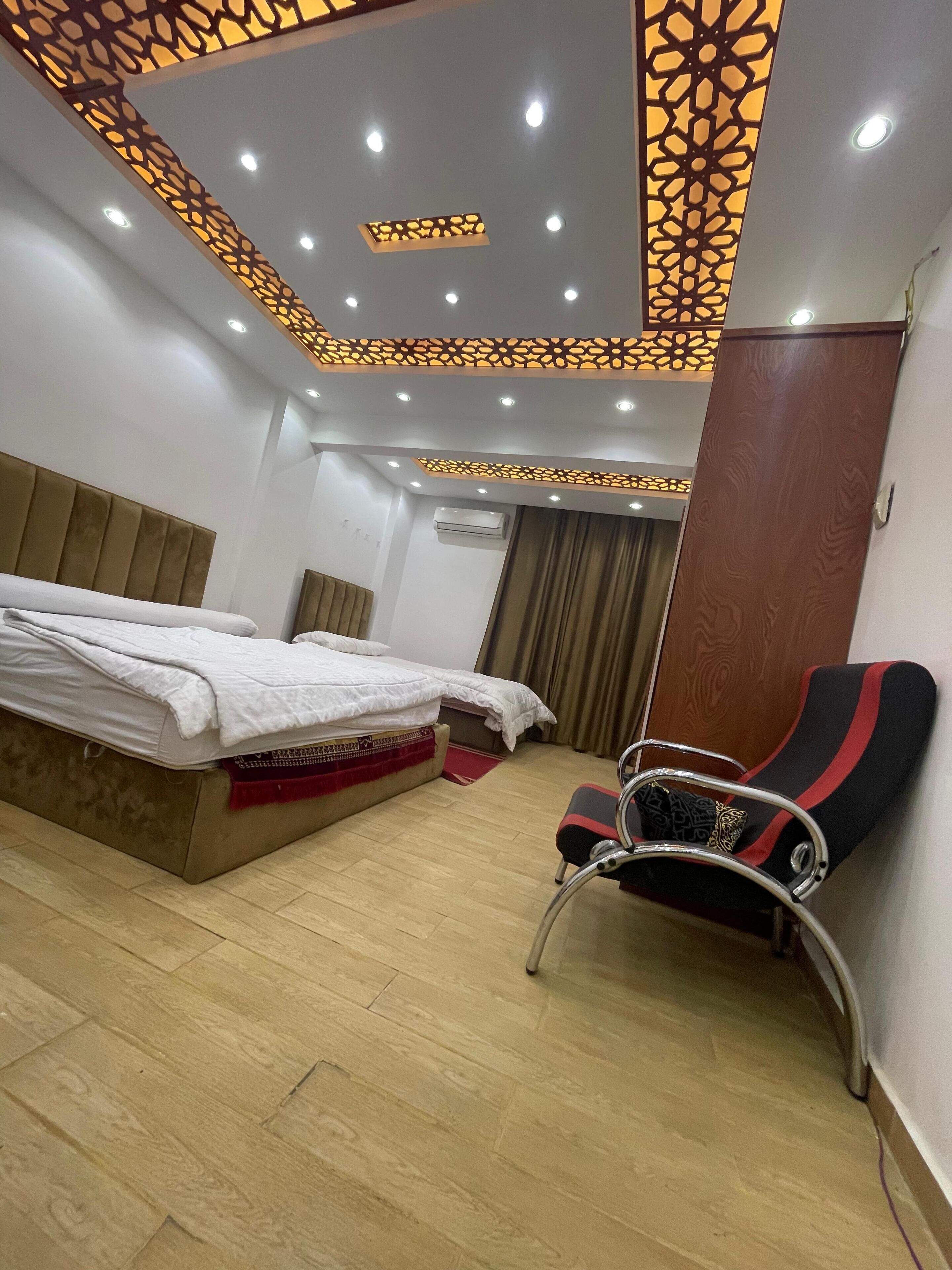 Una habitación de hotel con cama, una silla, piso de madera e iluminación decorativa en el techo.