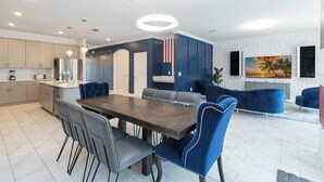 A modern kitchen with a dining area, featuring a large wooden table and blue upholstered chairs. - Fantastic Home 7BR/5BA with Private Pool • Storey Lake Resort [SL2648] (Kissimmee)